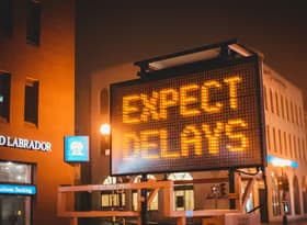 Illuminated "Expect Delays" sign in city streets at night, cautioning drivers.