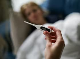 Hand holding a digital thermometer with blurred background of a sick person.