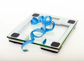 A digital glass weighing scale with a blue measuring tape, symbolizing weight management.